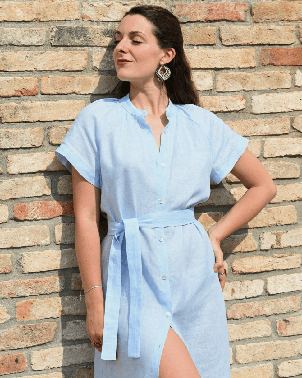 Modella in un vestito di lino azzurro da donna, con spacco laterale e cintura. Ideale per un look estivo e versatile, riflette la qualità del lino Made in Italy.