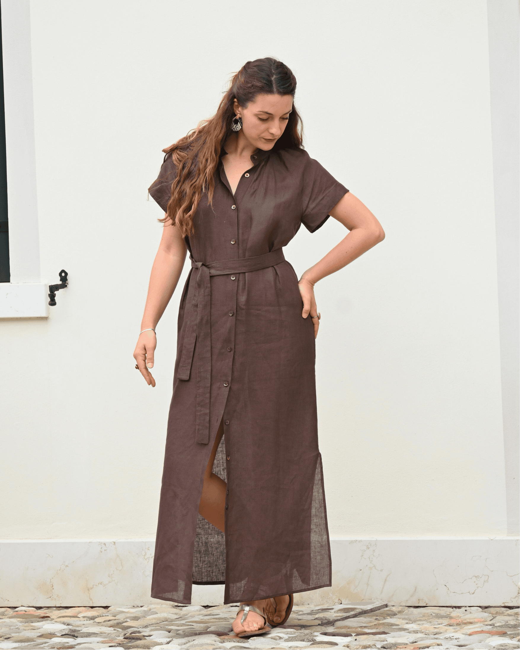 Modella in un vestito di lino marrone chocolato da donna, con spacco laterale e cintura. Ideale per un look estivo e versatile, riflette la qualità del lino Made in Italy.