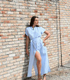 Modella in un vestito di lino azzurro da donna, con spacco laterale e cintura. Ideale per un look estivo e versatile, riflette la qualità del lino Made in Italy.