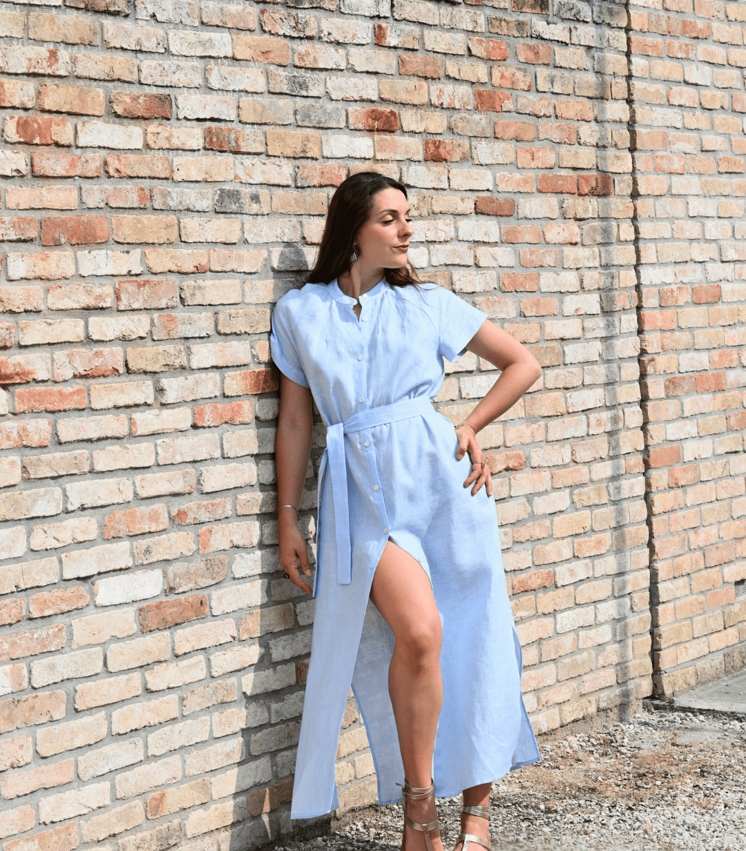 Modella in un vestito di lino azzurro da donna, con spacco laterale e cintura. Ideale per un look estivo e versatile, riflette la qualità del lino Made in Italy.